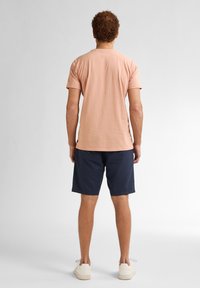 Camiseta de algodón en color durazno claro, de mangas cortas, con un corte relajado, combinada con pantalones cortos azul marino y zapatillas crema. Diseño sencillo, sin logotipos ni patrones visibles.