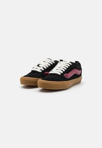 Baskets en suede noir avec accent en vagues roses, dotées de lacets blancs et d'une semelle en caoutchouc gomme. Le design comprend un profil bas et un bout arrondi.
