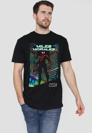 Man wearing black T-shirt featuring Miles Morales Spider-Man graphic with cityscape background and Marvel logo, paired with blue jeans.