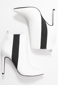 Botines de tacón alto blancos con paneles laterales de elastano negros, punta afilada y un diseño elegante. Los acentos de tela texturizada crean contraste.