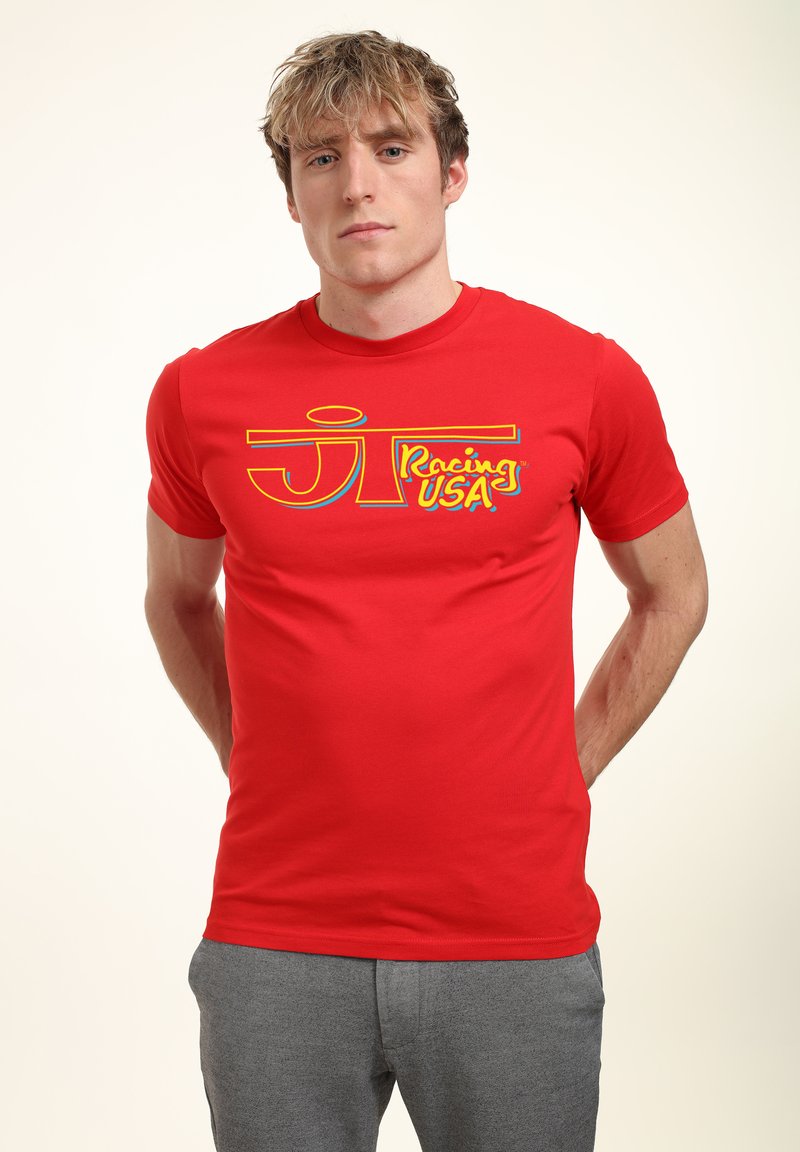 Rød bomulds t-shirt med et stort, multicolor grafik, der står "JT Racing USA" i en fed, stiliseret skrifttype. Korte ærmer og rund hals.