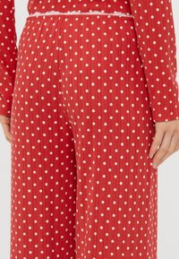 Roter strukturierteter Stoff mit weißen Punkten, elastischem Bund und Spitzenbesatz am oberen Rand. Sichtbare seitliche Nahtdetails.