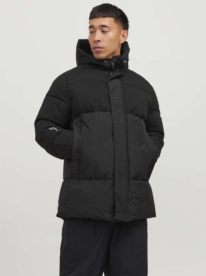 Zwarte gewatteerde winterjas met een capuchon, voorzien van een ritssluiting aan de voorkant, grote gewatteerde delen en zijzakken. Glad oppervlak, minimalistisch design.