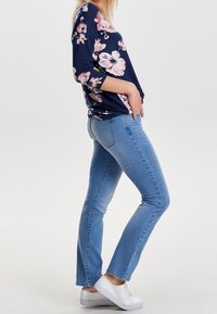 Marineblaues Langarmoberteil mit pinkem Blumenmuster, kombiniert mit hellblauen geraden Jeans und weißen Sneakers. Glatte Stofftextur und lässige Passform.