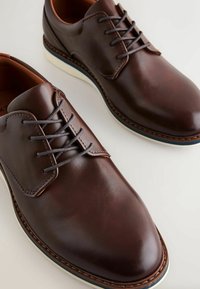 Bruine leren nette schoenen met een gladde afwerking, voorzien van vetersluiting, een afgeronde neus, contrasterende stiksels en een witte zool.