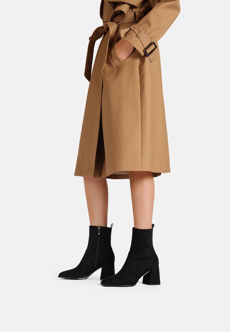 Stivali neri alla caviglia in un materiale liscio simile alla suede con tacco a blocco. Presentano una cerniera laterale e una silhouette snella.