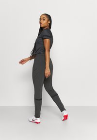 Donkergrijze sportoutfit met een kortgeschouderde top en strakke broek, met zwarte accenten, een gladde textuur en sportieve schoenen.