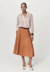 Crème en bruine gestreepte button-up shirt, roestkleurige, knielange rok met een gladde textuur, en witte open teen hakken. Gouden manchetten armband accent.