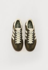 Brun och krämfärgad sneaker med en mesh-övre del, tre vita ränder och en vadderad krage. Innersulan har ett blommönster. Gummisula.