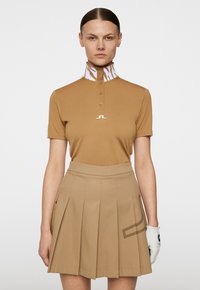 Brązowa koszulka polo z wysokim kołnierzem, ozdobiona wzorem w białe paski tigrze, w połączeniu z dopasowaną plisowaną spódnicą i białą rękawicą golfową.