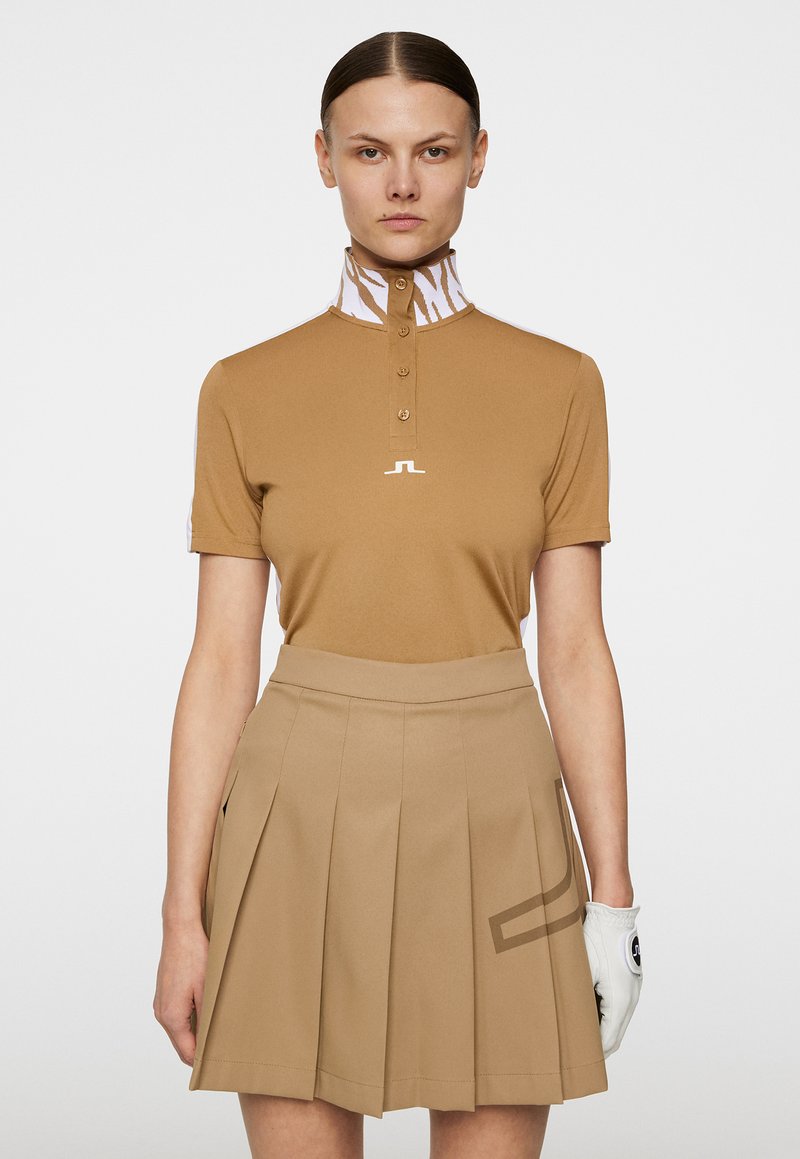 Brązowa koszulka polo z wysokim kołnierzem, ozdobiona wzorem w białe paski tigrze, w połączeniu z dopasowaną plisowaną spódnicą i białą rękawicą golfową.