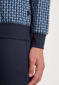 Navyblauwe sweatshirt met een geometrisch patroon in lichtblauw, met ribgebreide manchetten en zoom. Het materiaal lijkt zacht en gestructureerd.