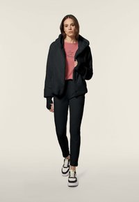 Giacca in pile nera con cappuccio, abbinata a una maglietta corta rosa, pantaloni neri e sneaker in bianco e nero. Include guanti senza dita.