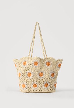 Sac fourre-tout beige crocheté avec motifs de marguerites orange et blanches, bords festonnés et deux longues poignées tressées.