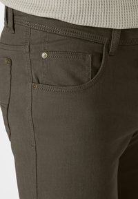 Dark olive green trousers with a textured fabric, five-pocket design, and gold-tone hardware accents. Visible stitching along the seams.