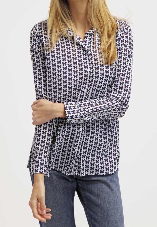 Långärmad skjorta gjord av ett lätt tyg, med vit bakgrund och lila fjärilstryck samt knäppning.