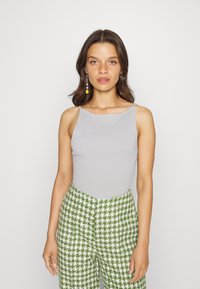 Camisola cinza de alças finas com vazadas, combinada com calças largas em padrão pied-de-poule verde e branco. Textura suave, silhueta ajustada.