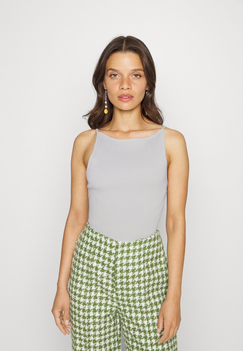 Camisola cinza de alças finas com vazadas, combinada com calças largas em padrão pied-de-poule verde e branco. Textura suave, silhueta ajustada.