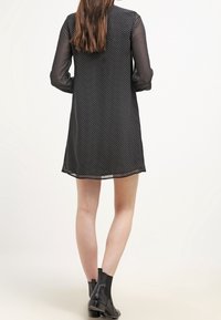 Vestito nero a pois con maniche lunghe trasparenti e vestibilità ampia, caratterizzato da uno scollo rotondo e un orlo che arriva sopra il ginocchio.