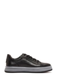 Zapatilla de cuero negro con un acabado suave, que cuenta con seis agujeros para los cordones, una suela de goma gris y un diseño de punta redonda.
