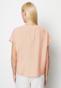  ferskenfarvet bluse med korte ærmer, rund halsudskæring, let krøllet stof og lige kant med detalje på bagsømmen.