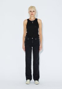 Schwarzes Tanktop, getragen mit dunklen Jeans in geradem Schnitt, Fünf-Taschen-Design und silbernen Hardware-Details.