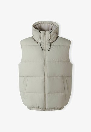 Světlý béžový puffový vest s vysokým límcem, předním zipem a stahovacími šňůrkami. Obsahuje horizontální prošívaný design a dvě boční kapsy.
