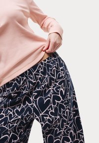 Marineblaue Schlafanzughosen mit einem rosa Herzmuster, elastischem Bund und leichtem Stoff, kombiniert mit einem hellrosa Langarmshirt.