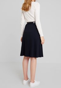 Navy flared skirt dengan tekstur halus, pinggang pas, dan lipatan halus. Dipadukan dengan atasan lengan panjang ringan dan sepatu sneakers putih.