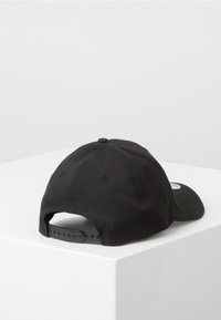 Gorra de béisbol negra con visera curva, hecha de algodón. Presenta un cierre a presión de plástico y orificios de ventilación en la parte superior.