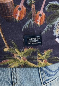 Námořnické tričko s potiskem tropických palem a hudebních nástrojů, včetně kytar. Na spodním lemu se nachází modrá visačka s nápisem "Petrol Ind".