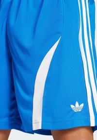Shorts de sport bleus en tissu lisse avec des accents blancs sur les côtés, des détails en mesh et un petit logo blanc sur la jambe inférieure.