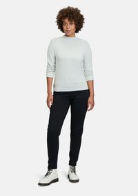 Ljust grå, långärmad tröja med en figursydd design, kombinerad med svarta byxor och vita snörskor. Slät textur, minimala accenter.