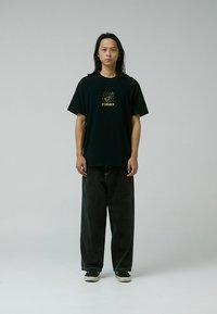 Camiseta negra con un gráfico dorado central que dice "FORMER." Combinada con pantalones de mezclilla oscuros de corte holgado y zapatillas negras. Diseño simple.