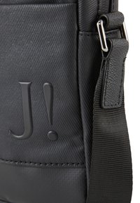 Borsa a spalla in tessuto nero con superficie testurizzata, logo impresso e tracolla regolabile. Elementi hardware con finitura metallica.