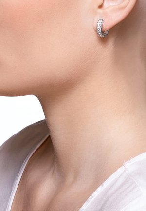 Silberne Ringohrringe mit geschwungenem Design, verziert mit einer Reihe klarer, funkelnder Steine entlang der Vorderkante.