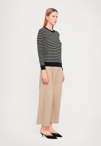 Pull rayé noir et blanc en matière légère, col rond, associé à un pantalon large beige et des escarpins noirs à bout pointu.