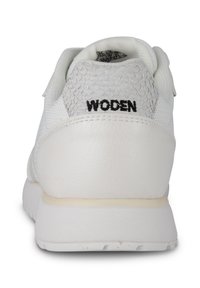 Zapatilla blanca con un diseño de cuero texturizado y malla, presenta un patrón circular, cuello acolchado y una marca "WODEN" en negro en el talón.