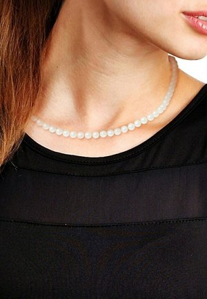 Collier de perles blanches givrés, de forme ronde uniforme, enfilé sur un fil fin, reposant sur un haut noir, mettant en valeur la texture lisse et la brillance.