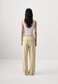 White ribbed tank top with a deep V-back paired with high-waisted yellow trousers featuring front pockets and cuff buttons at the hems.