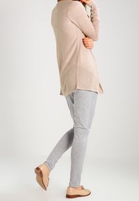 Light pink knitted cardigan with a longer back, paired with gray tapered pants and beige shoes. Features textured details on the cardigan.