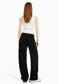 Czarne spodnie cargo z szerokimi nogawkami, dwoma bocznymi kieszeniami i dopasowanym pasem, w zestawie z białym bezrękawnikem. Gładka tekstura materiału.