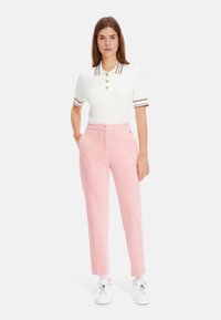 White knitted polo shirt with short sleeves, featuring horizontal stripes and gold buttons. Pink tailored trousers with a straight cut.