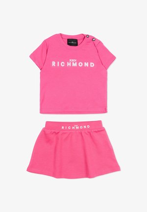 Ensemble enfant deux pièces rose avec un haut à manches courtes et une jupe, tous deux avec le logo blanc imprimé "John Richmond".