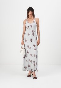 Lang, ermiddels maxi-kjole i lysegrå med maroon blomstertrykk. Laget av et flowy stoff, har v-hals og en subtil silhuett.