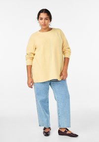 Maglione a maglia giallo chiaro con vestibilità ampia, polsini a coste e motivo strutturato. Abbinato a jeans a gamba larga a righe azzurre chiare e scarpe basse scure.