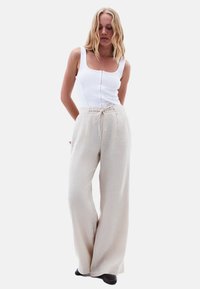 Débardeur blanc à côtes avec détails de boutons associé à un pantalon en lin beige ample avec taille à cordon et jambes larges.