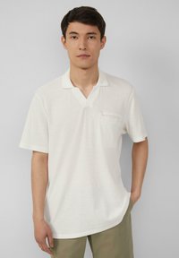 Witte polo met korte mouwen en een v-hals, van gestructureerde stof, met een klein borstzakje. Relaxte pasvorm met rechte zoom.