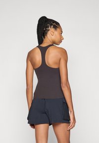Brun sport tanktop med racerrygdesign, glat tekstur og tætsiddende silhuet, parret med mørke shorts med sidelommer.