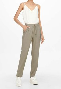 Lekka bluzka w kremowym kolorze z falbaniastym dekoltem, zestawiona z luźnymi spodniami w oliwkowym odcieniu, które mają boczne kieszenie, elastyczny pas oraz ściągacze na nogawkach.